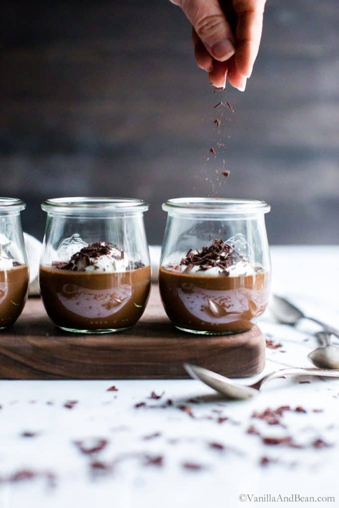 Chocolate Pots de Crème on a serving board being sprinkled with chocolate. 