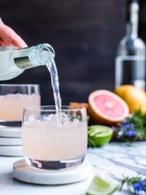 Pouring ginger beer into fresh grapefruit Moscow mules in a cocktail glass.