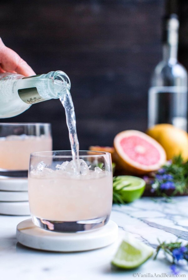 Pouring ginger beer into fresh grapefruit Moscow mules in a cocktail glass.