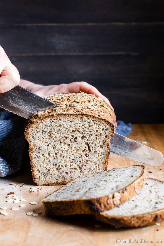 A hand with a knife cutting a loaf of gluten free sourdough bread. 