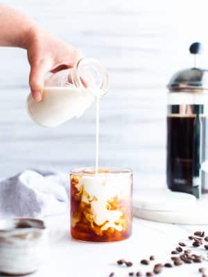 Pouring milk into a glass of iced cold brew coffee.