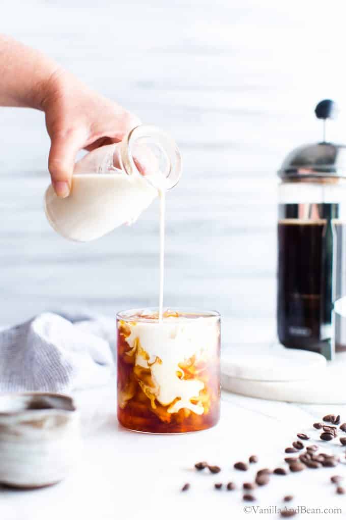 Pouring milk into a glass of iced vanilla cold brew coffee. 