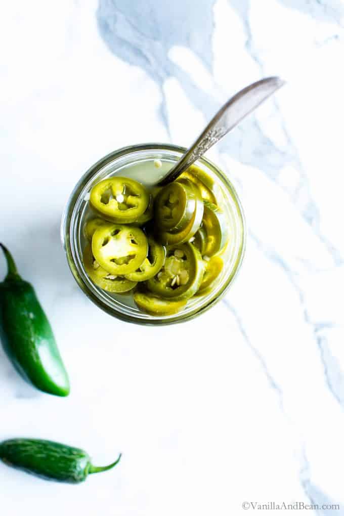 Pickled jalapeños in a jar with a fork stuck in it. 