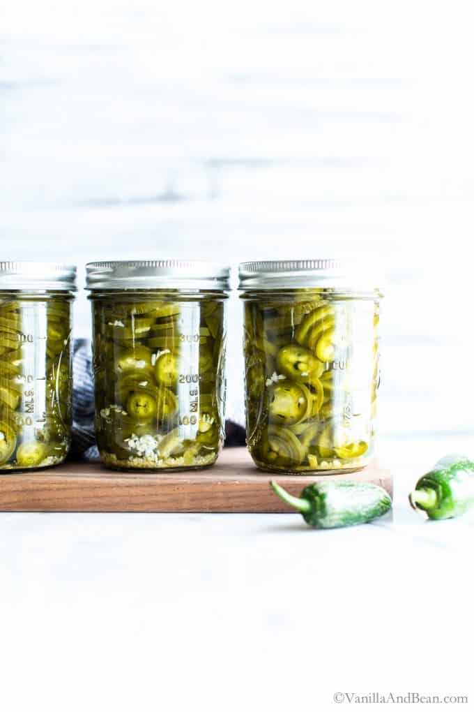 Jars filled with canned jalapeno peppers setting on a board. 