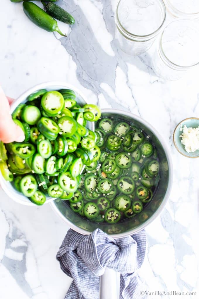 Pouring sliced jalapeños in a pan with brine.