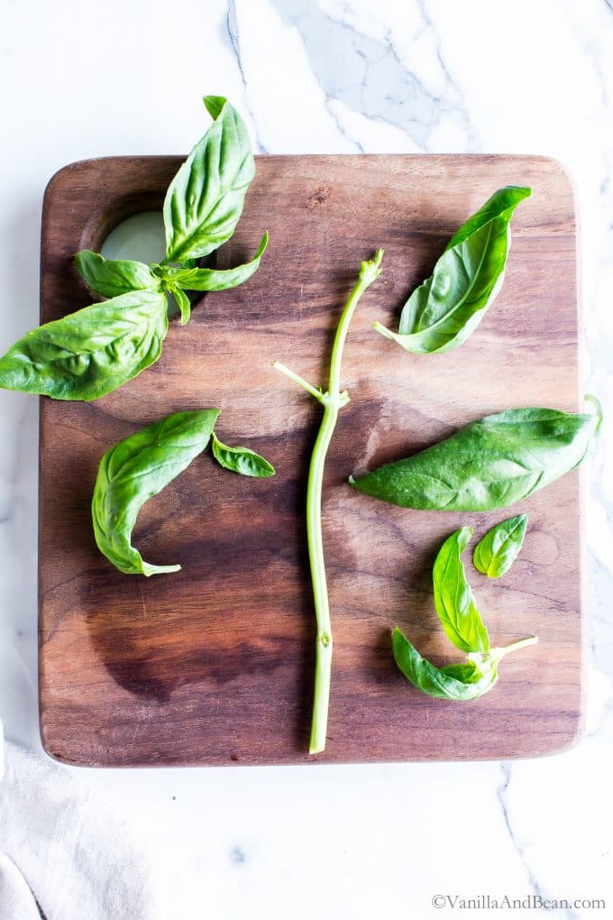 Removing basil leaves from the stem on a cutting board.