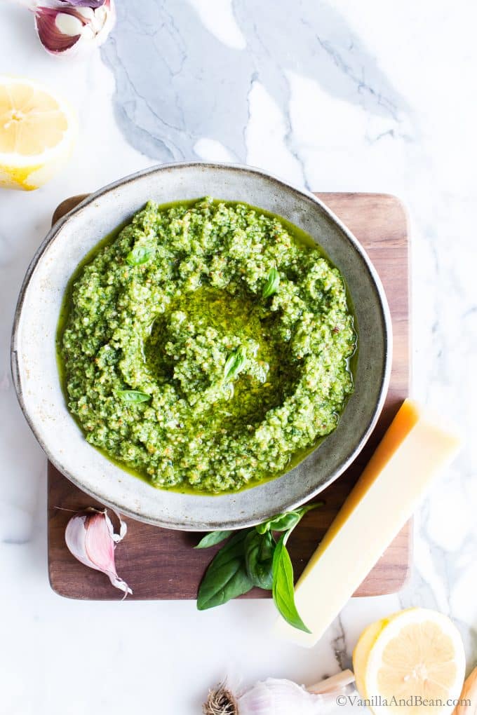 Lemon basil pesto in a bowl on a wood board with Parmesan cheese next to the bowl.