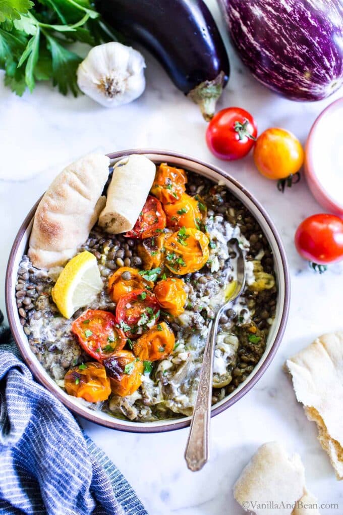 Mediterranean eggplant and lentils recipe in a bowl with a side of pita and a lemon wedge.