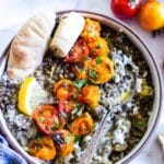 Mediterranean eggplant recipe in a bowl with a side of pita and a lemon wedge.