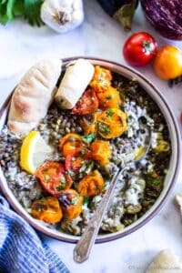 Mediterranean eggplant recipe in a bowl with a side of pita and a lemon wedge.