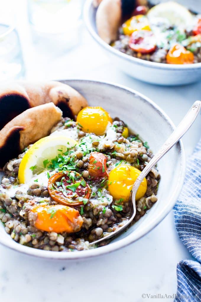 Lemon Garlic Lentils with Roasted Eggplant in a bowl served with Naan and a lemon wedge.
