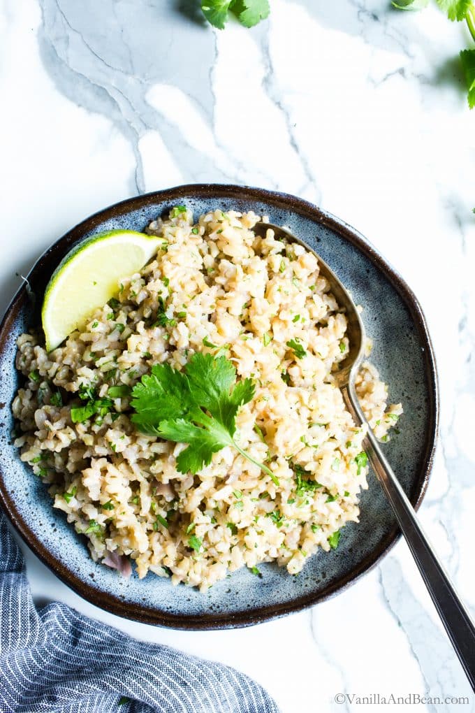 Cilantro brown rice in a bowl with a lime wedge and cilantro. 