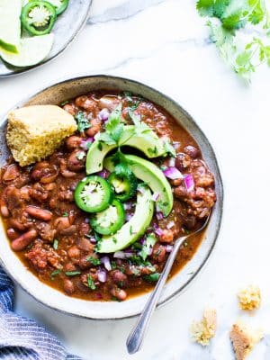 Vegetarian Chili in a bowl garnished with avocado, peppers and shared with cornbread.