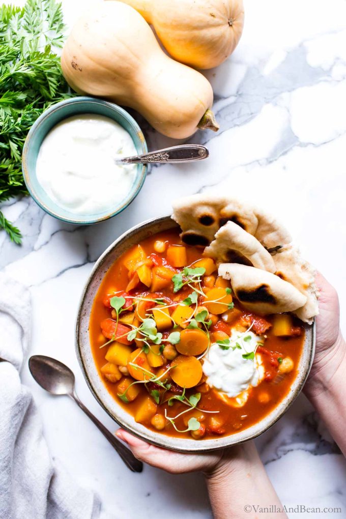 Butternut Squash Chickpea Stew in a bowl with hands holding the bowl. 