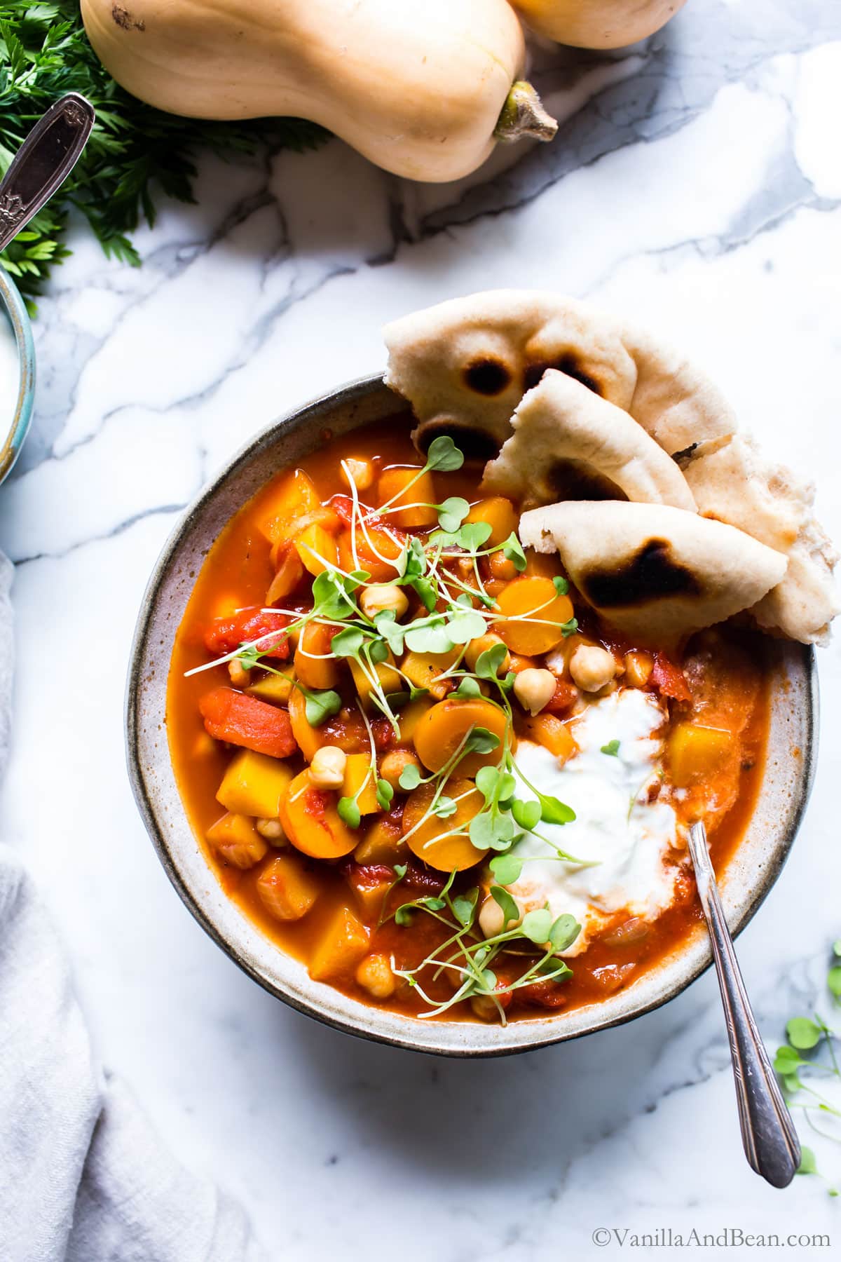 Moroccan Butternut Squash Stew topped with yogurt, microgreens and shared with Naan in a bowl.