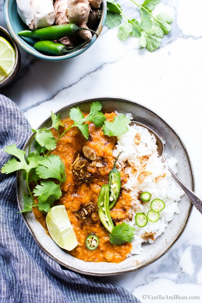 Red Curry Masoor Dal Recipe in a bowl with rice and garnished with cilantro and peppers. 