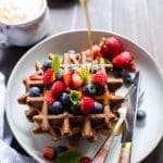 Gluten Free Sourdough Waffles on a plate topped with berries and syrup being poured over the top.