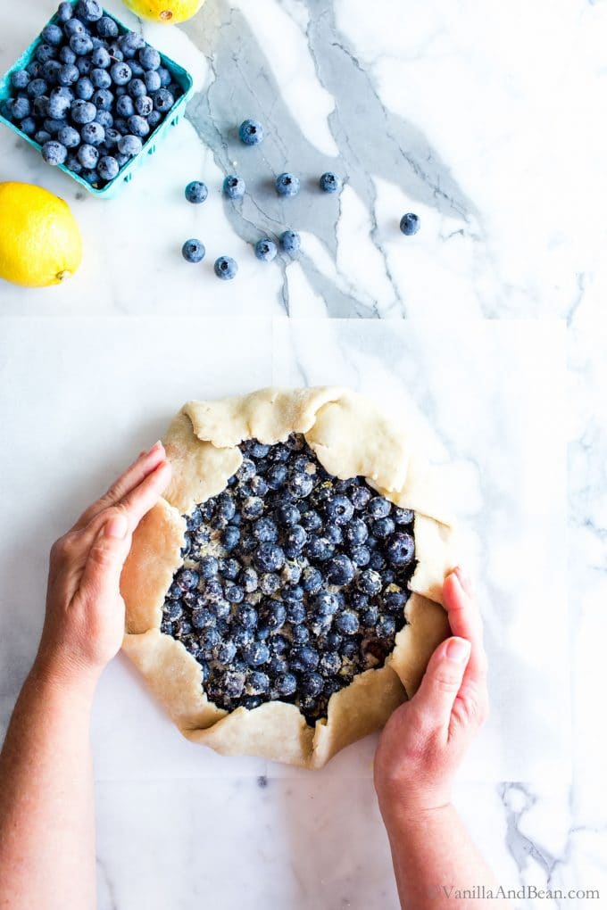 Hands securing the galette dough around the bleberries. 