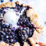 Blueberry Galette with ice cream melting in the center. One slice being pulled from the side.