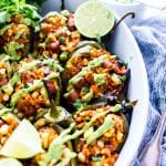 Stuffed Poblano Peppers in a roasting dish with avocado cream drizzled over the top.