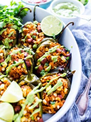 Stuffed Poblano Peppers in a roasting dish with avocado cream drizzled over the top.