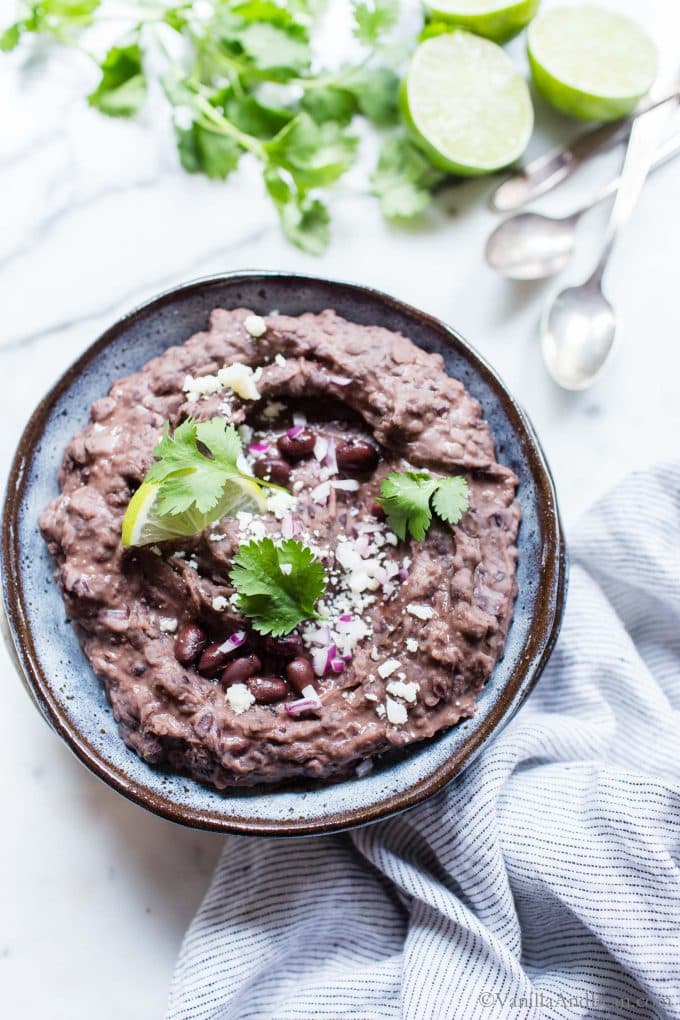 Refried Black Beans in a bowl garnished with lime, cilantro and fresh cheese.