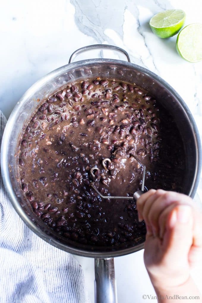 Mashing black beans in a pan to make refried black beans recipe.