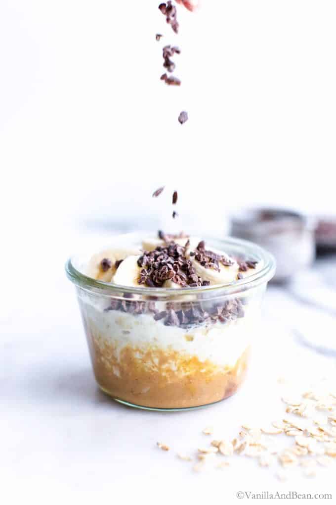Overnight oats with yogurt in a glass jar with peanut butter, banana and cocoa nibs.