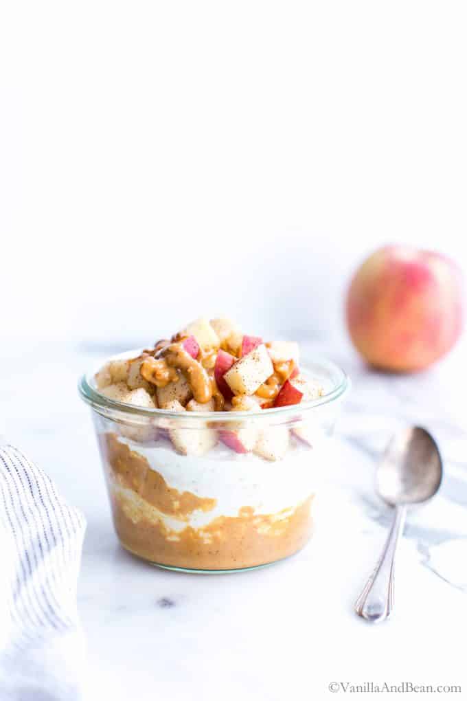 Overnight oats with yogurt in a glass jar with peanut butter, diced apple and cinnamon. 