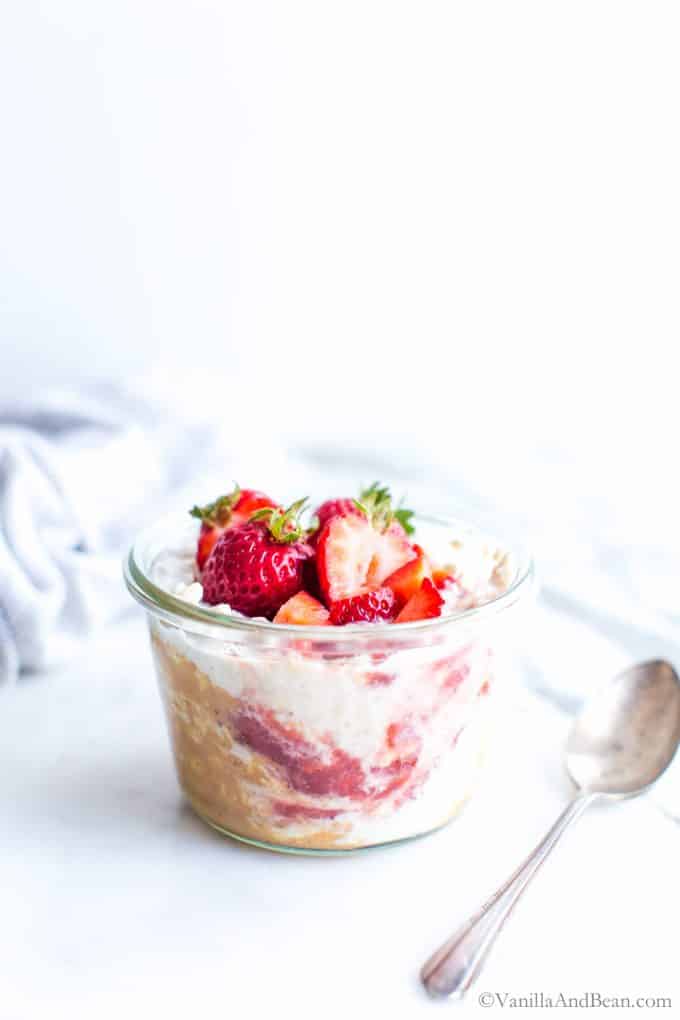 Overnight Oats Recipe with peanut butter, jam and fresh strawberries in a glass jar, ready to eat.