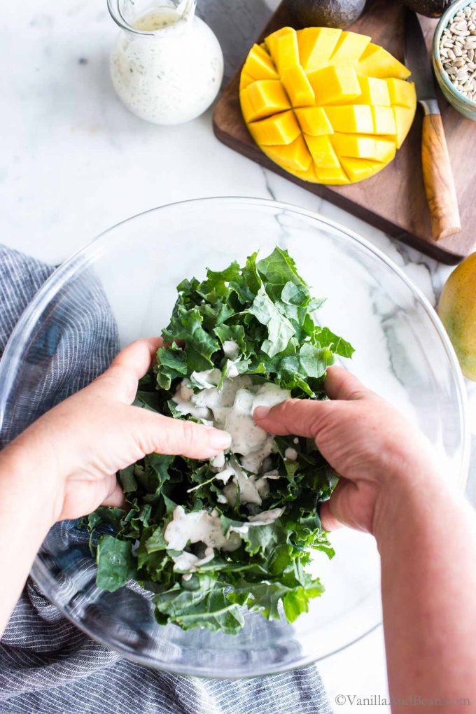 Massaging kale with ranch dressing in a bowl.
