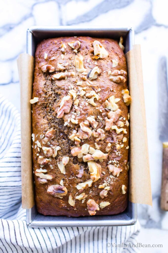 Close up of banana bread brown sugar in a loaf pan sprinkled with walnuts.