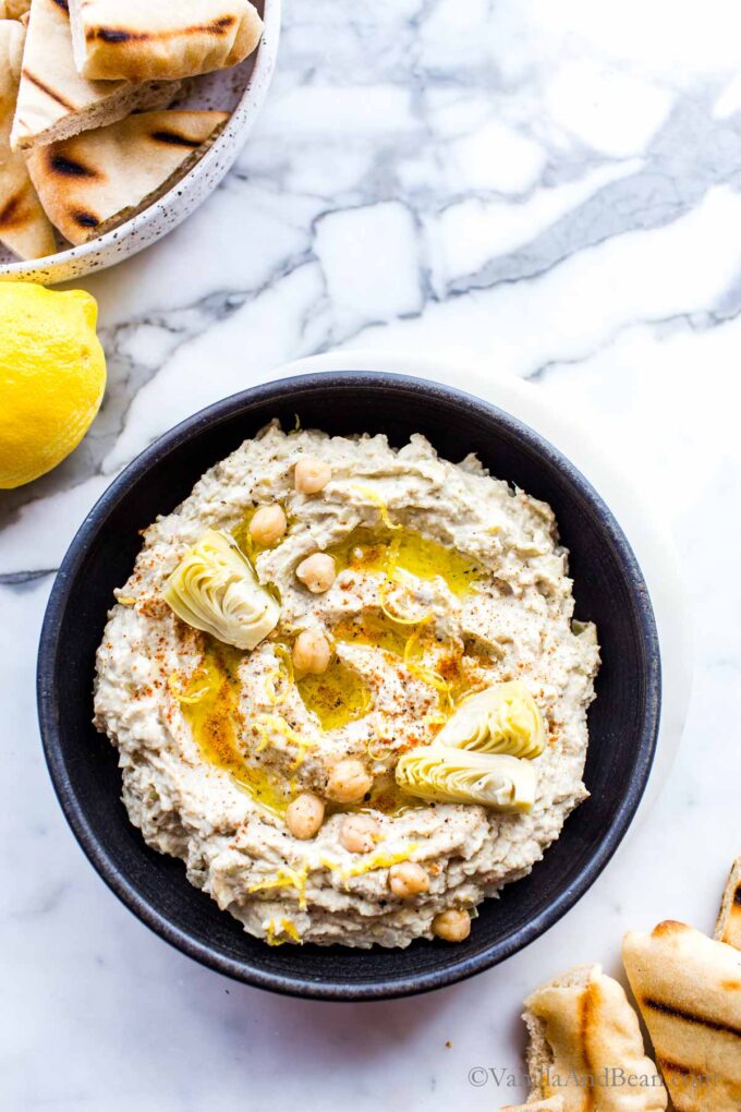 Close up of artichoke hummus dip in a bowl garnished with artichoke, chickpeas and olive oil.