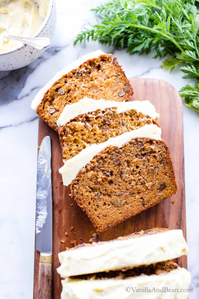 Carrot bread iced with orange cream cheese frosing on a cutting board with three pieces sliced.