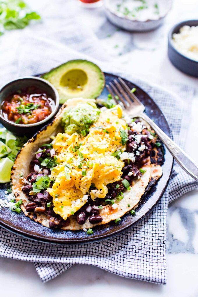 Breakfast tacos huevos rancheros on a plate with scrambled eggs and beans.