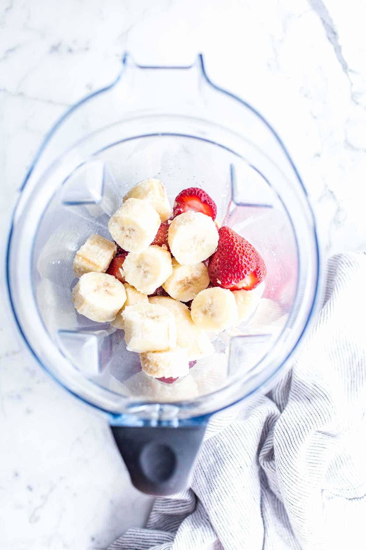 Bananas, strawberries and milk in a blender pitcher.