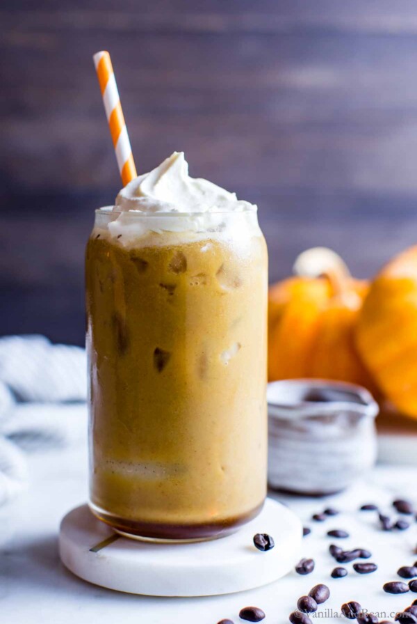 Iced pumpkin spice latte in a glass topped with whipped cream with a straw in the glass.