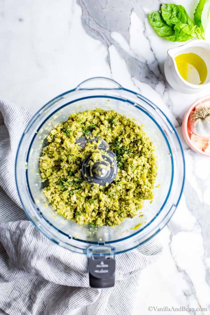Green tapenade in a work bowl of a food processor, after processing.
