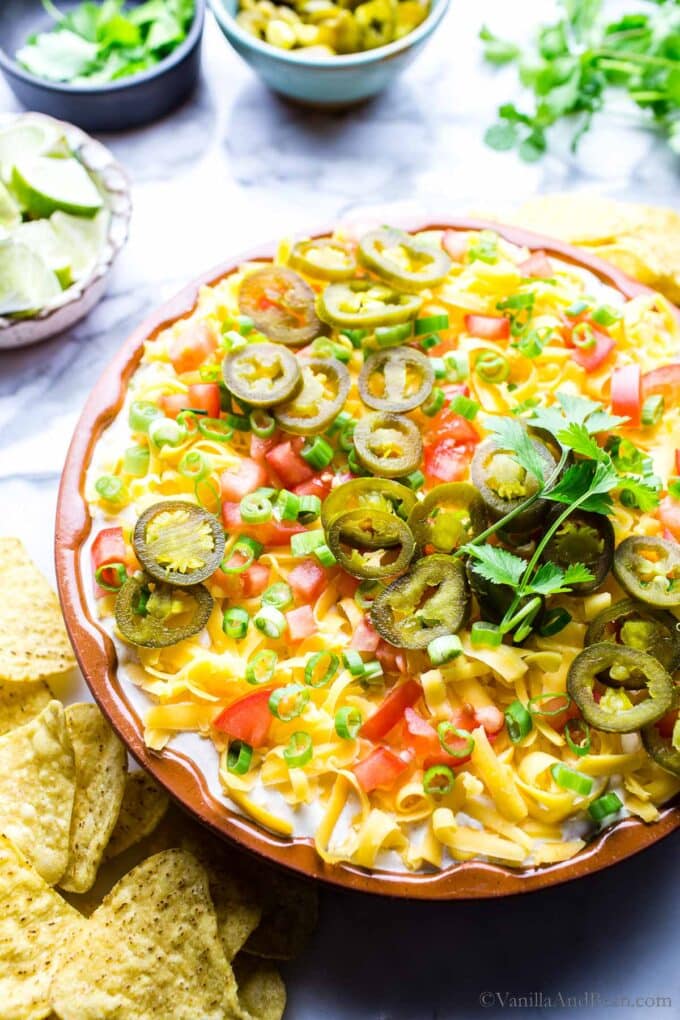 5 layer dip in a plate garnished with jalapenos and cilantro, surrounded by tortilla chips.