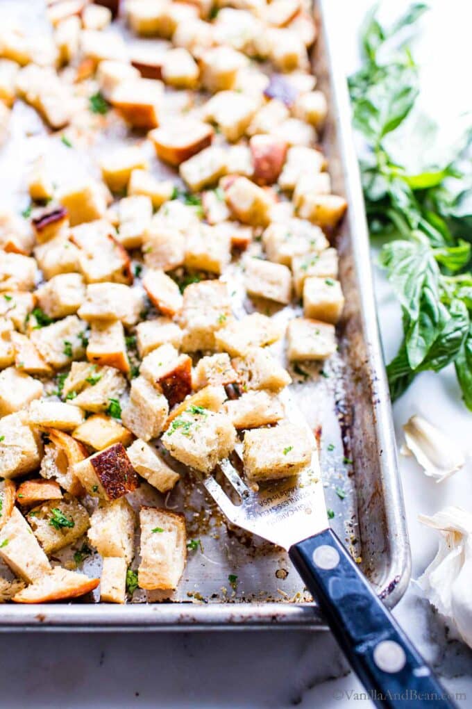 Homemade Sourdough Croutons on a sheet pan with a spatula garnished with herbs and Parmesan cheese.