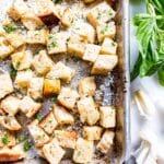 Homemade Sourdough Croutons on a sheet pan garnished with herbs and Parmesan cheese.
