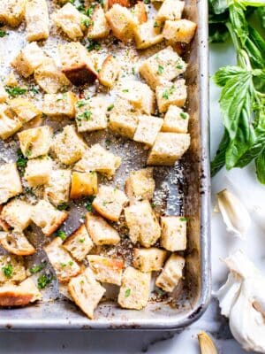 Homemade Sourdough Croutons on a sheet pan garnished with herbs and Parmesan cheese.