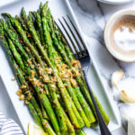 Pan fried asparagus recipe on a serving platter with a fork, garnished with lemon.