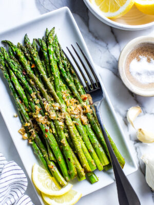 Pan fried asparagus recipe on a serving platter with a fork, garnished with lemon.