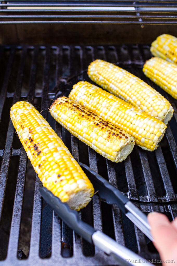 Sweet corn on the cob on the grill with tongs turning one of the ears.