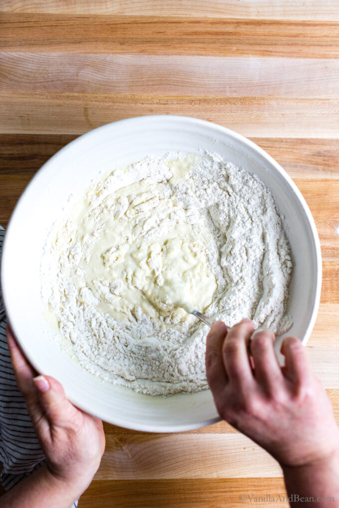Flour added to a bowl with wet ingredients for sourdough buns.
