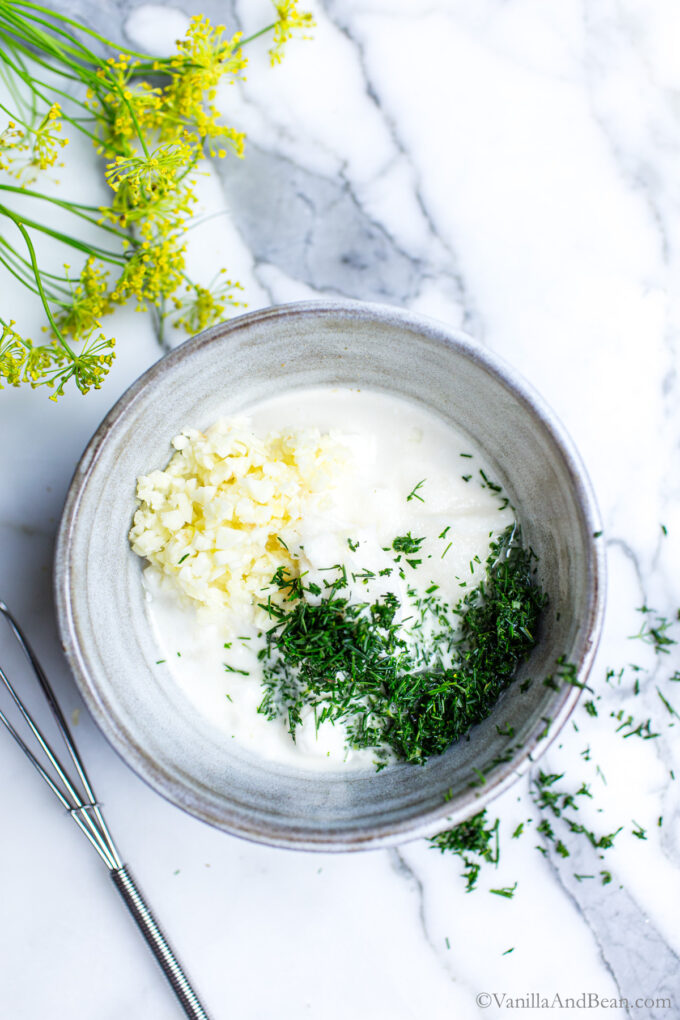 Creamy dill dressing in a bowl with dill spilled over the side.