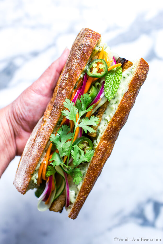 Vegan tofu banh mi sandwich being held by a hand.