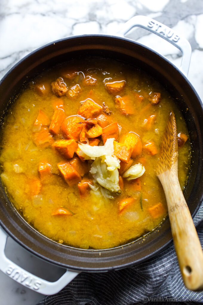 Sweet Potato Carrot Ginger Soup with roasted garlic ingredients in a Dutch Oven being stirred with a wooden spoon.