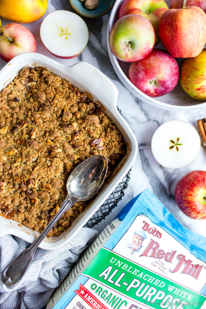 Dairy free apple crumble in a pan with Bob's Red Mill flour bag and apples all around.